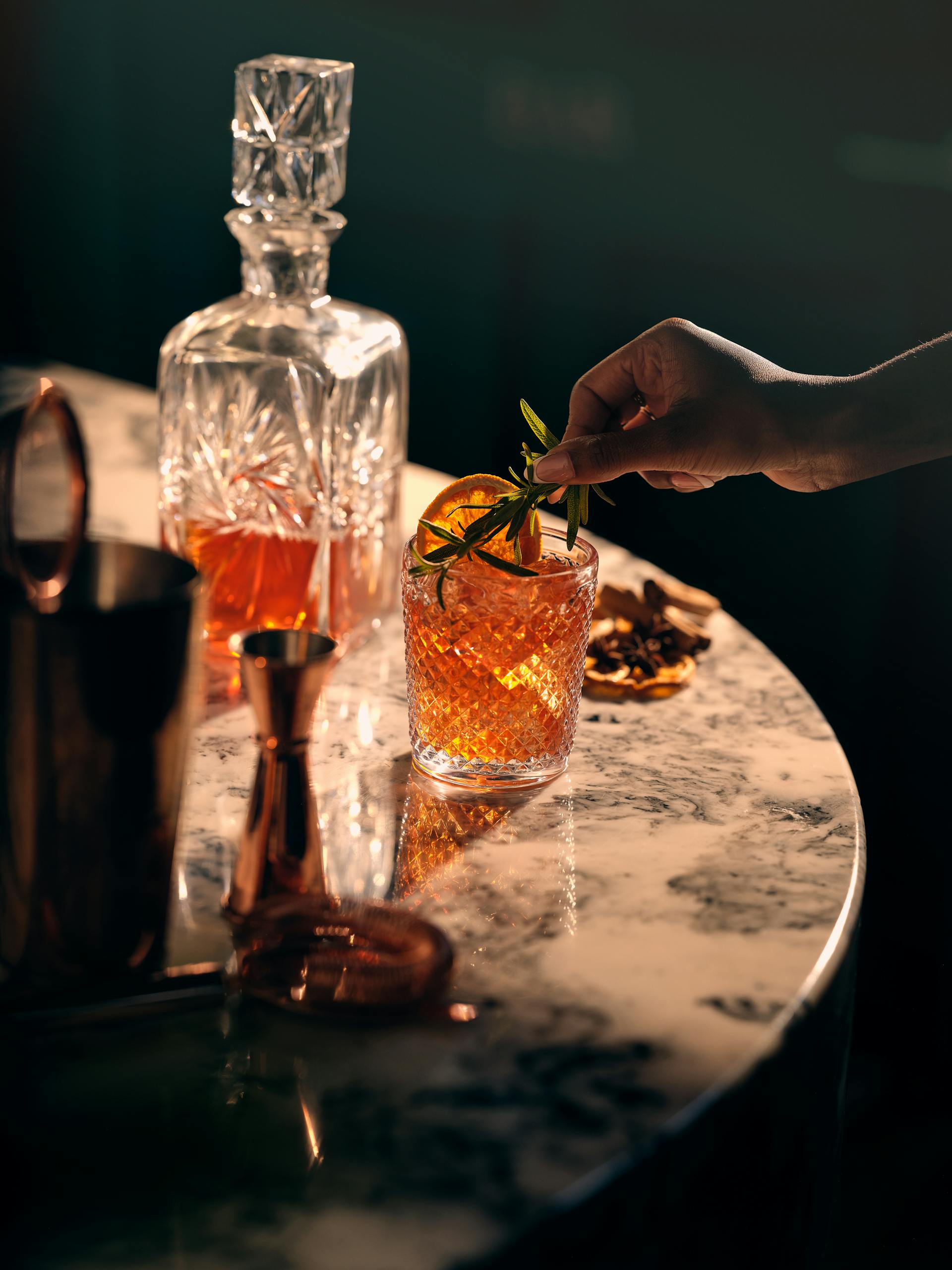 A stylish setup showcasing a hand garnishing a whiskey cocktail on a marble table.
