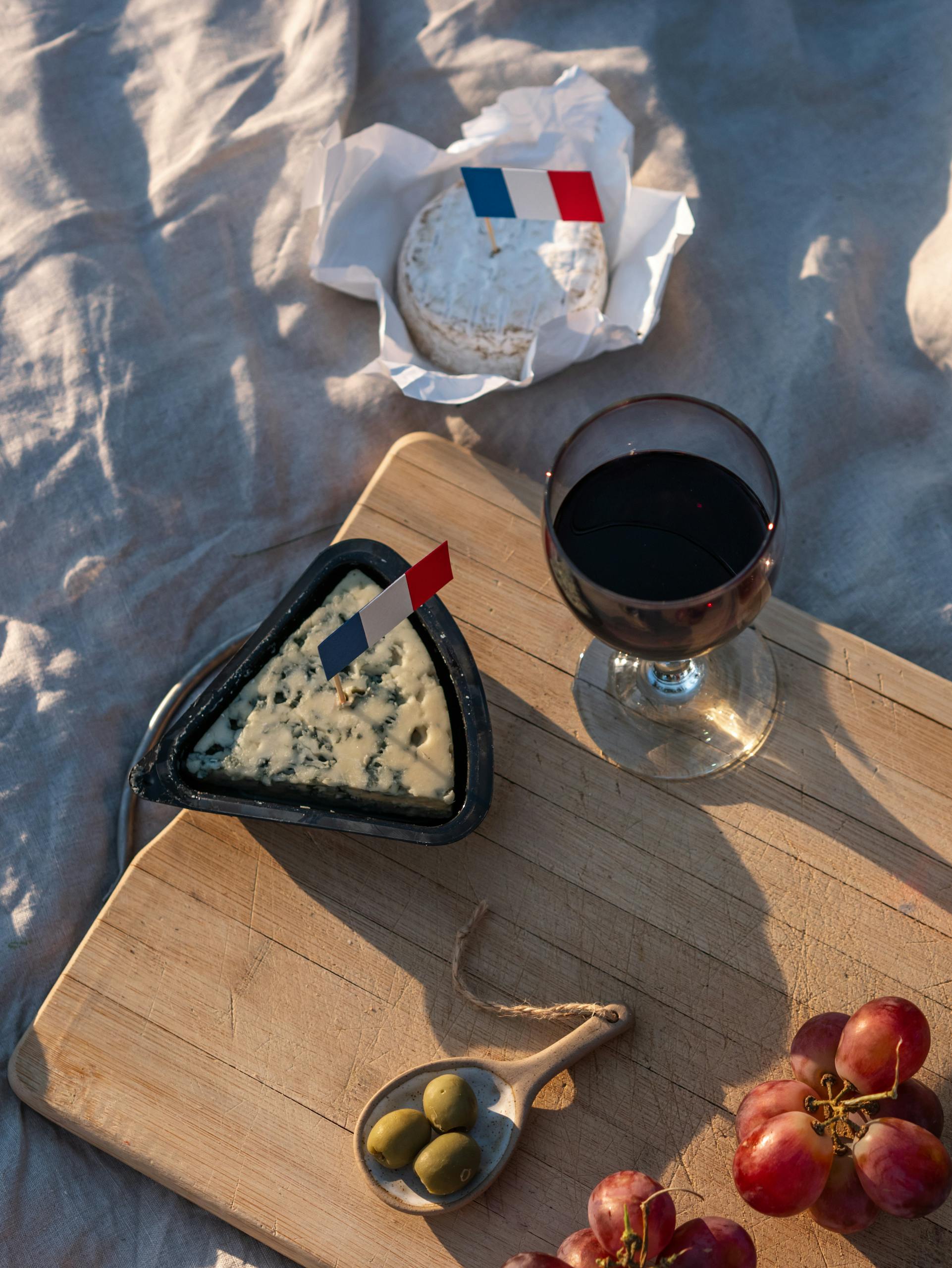 A cozy picnic showcasing French cheese, red wine, grapes, and olives on a wooden board.