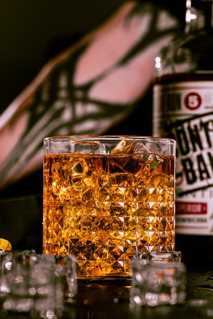 Close-up of a filled whiskey glass with ice and bottle background, dramatic lighting.