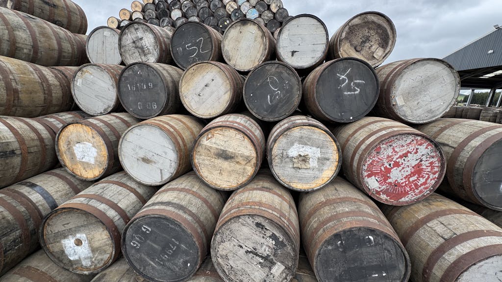 Rows of wooden barrels at a Scottish distillery under cloudy skies.
