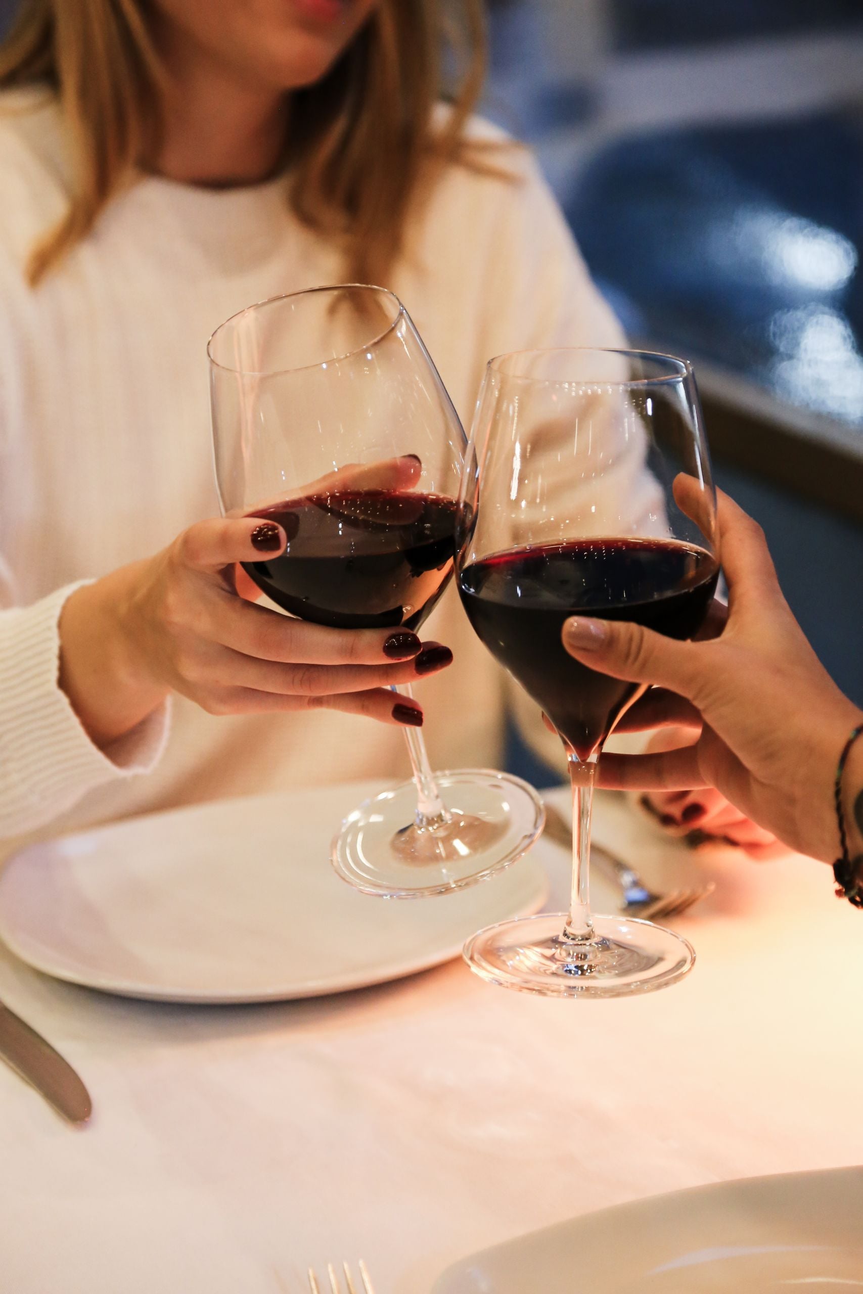 Two women clinking glasses of red wine in a warm restaurant ambiance, capturing a moment of celebration.